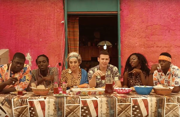 Six people eating at a long table before a pink wall, from Connection House