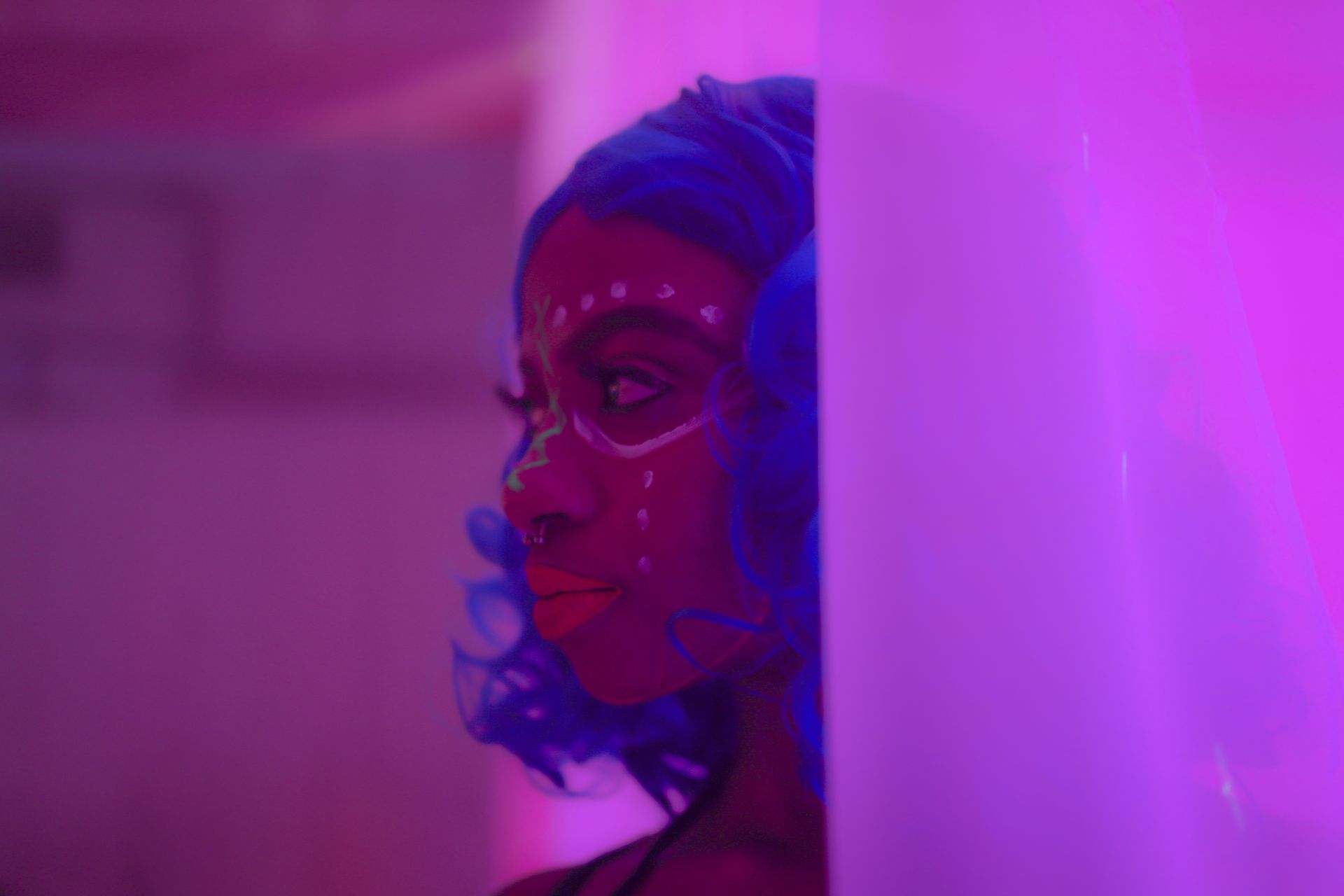 A dancer with blue hair and painted face in pink light